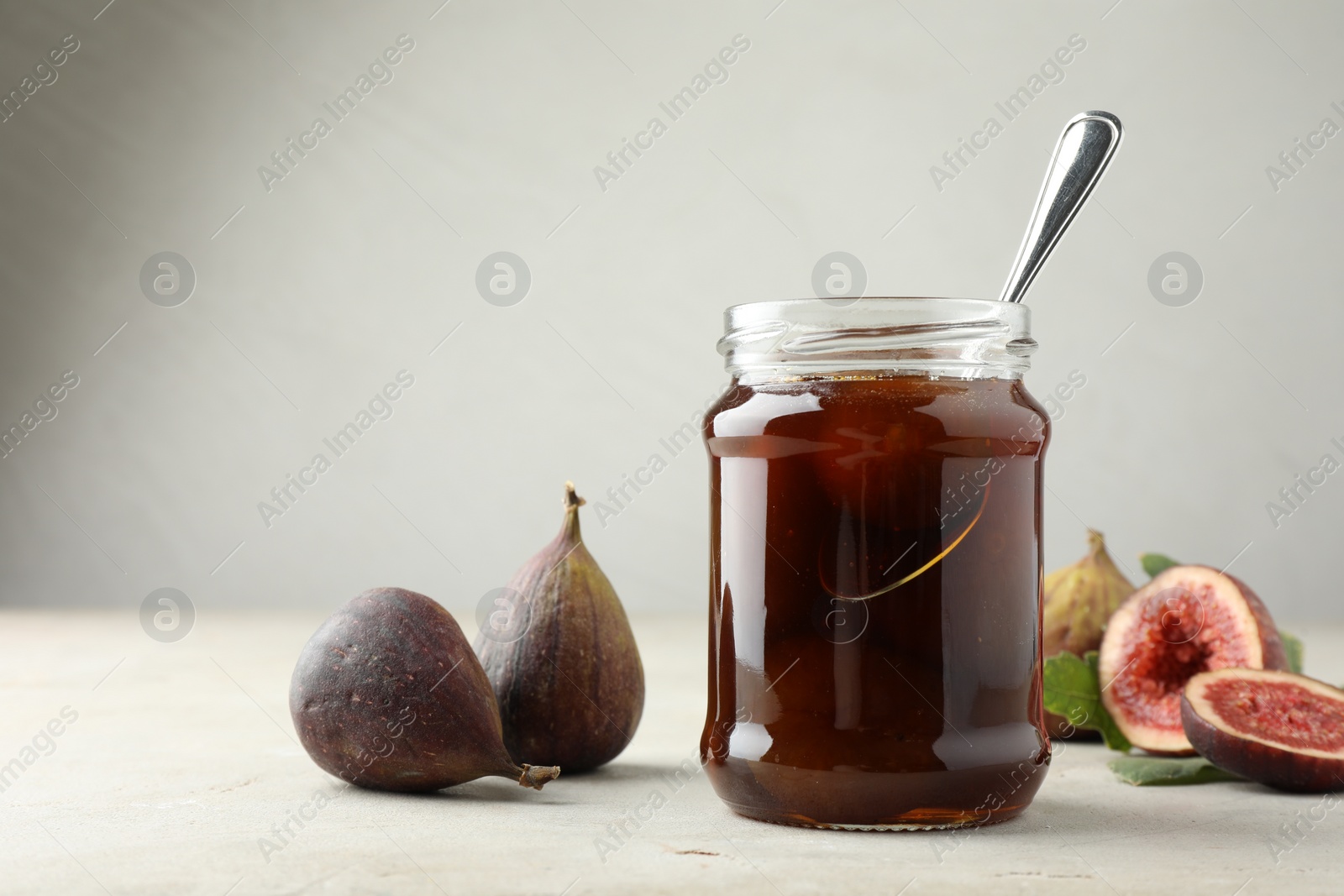 Photo of Jar of tasty sweet jam and fresh figs on light table, space for text
