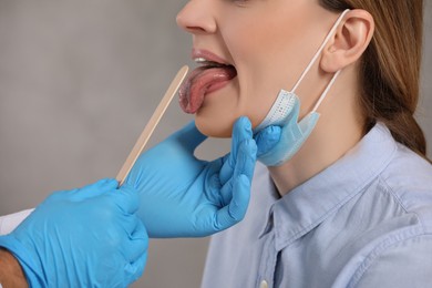 Photo of Doctor examining woman`s oral cavity with tongue depressor indoors, closeup