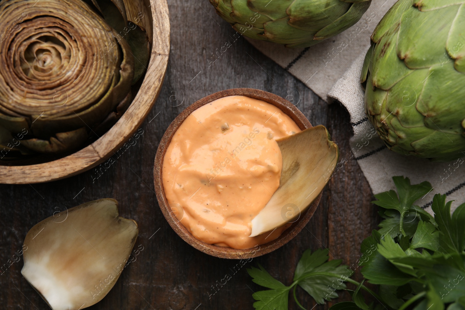 Photo of Delicious cooked artichoke with tasty sauce and fresh vegetable on wooden table, flat lay