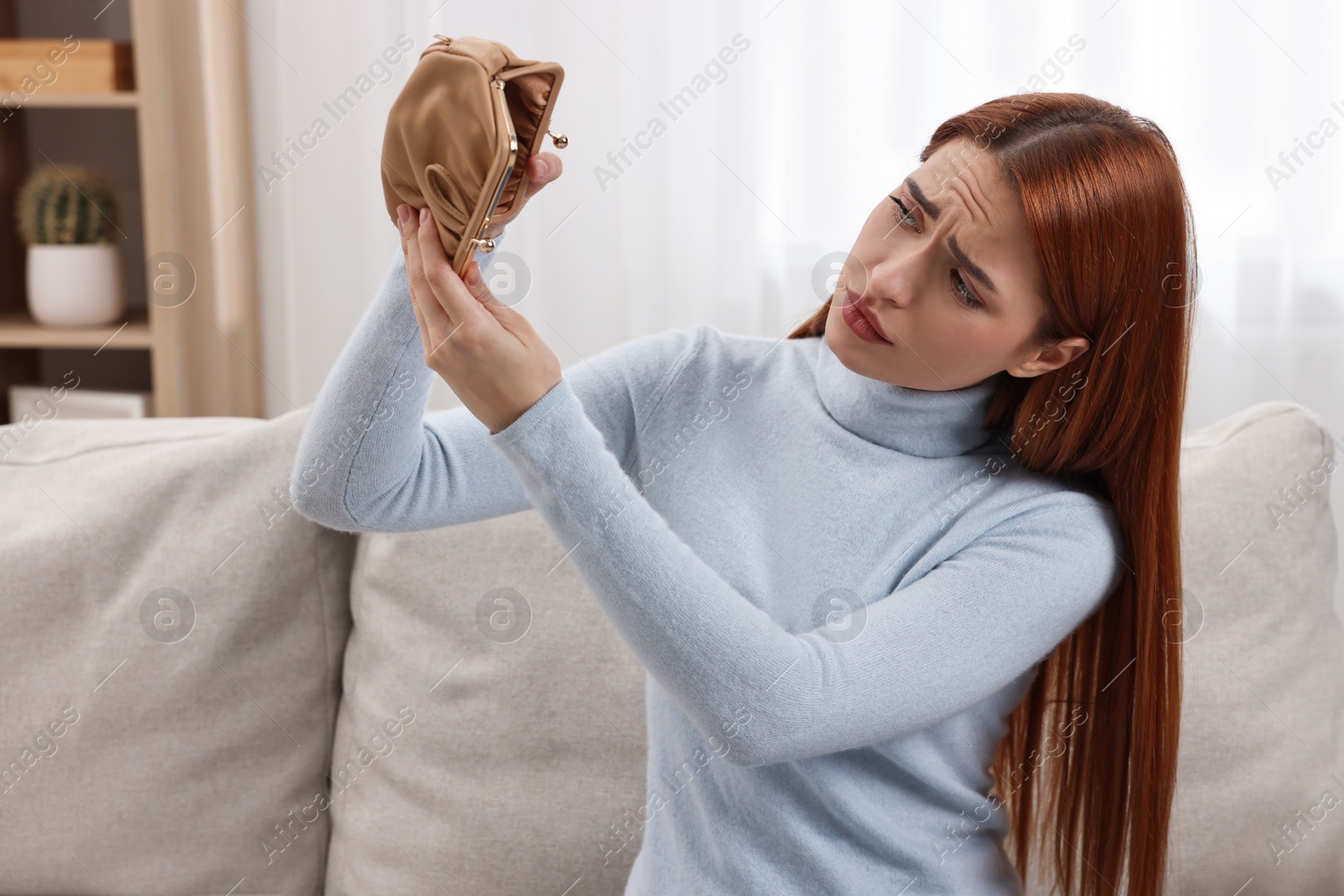 Photo of Upset woman with empty wallet on sofa indoors