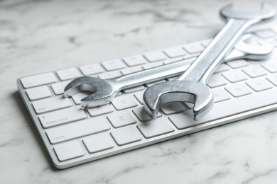 Photo of Keyboard and spanners on white marble table, closeup. Concept of technical support