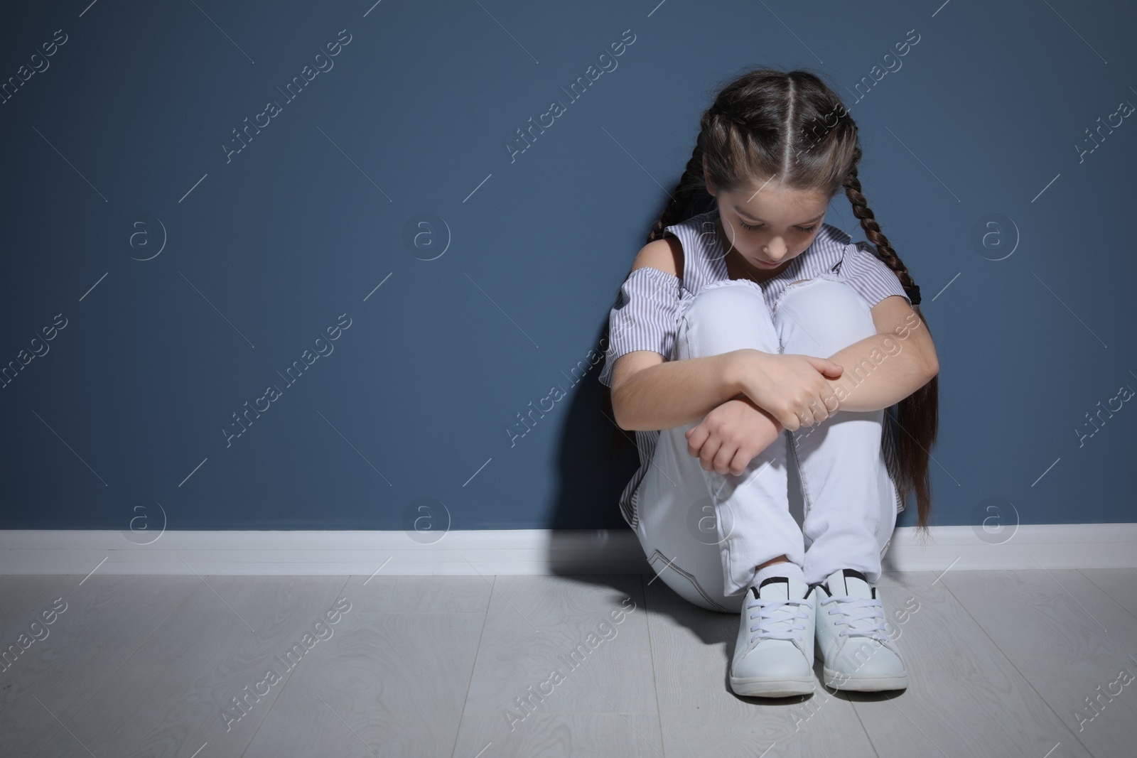 Photo of Depressed little girl sitting on floor indoors. Time to visit child psychologist