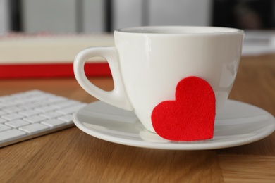 Photo of Cup with red heart and keyboard on wooden table, closeup. Valentine's day celebration