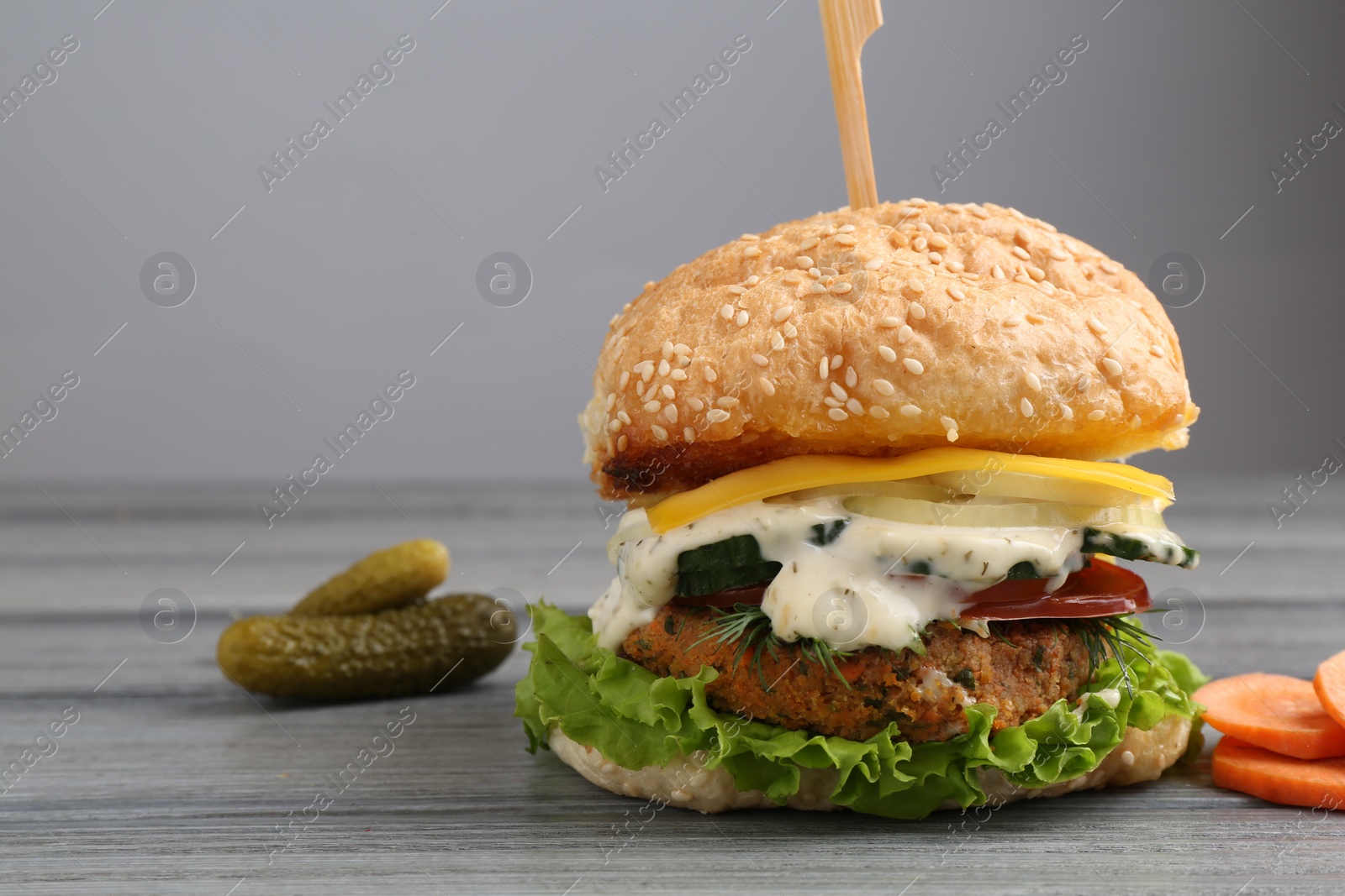 Photo of Delicious vegetarian burger and ingredients on grey wooden table