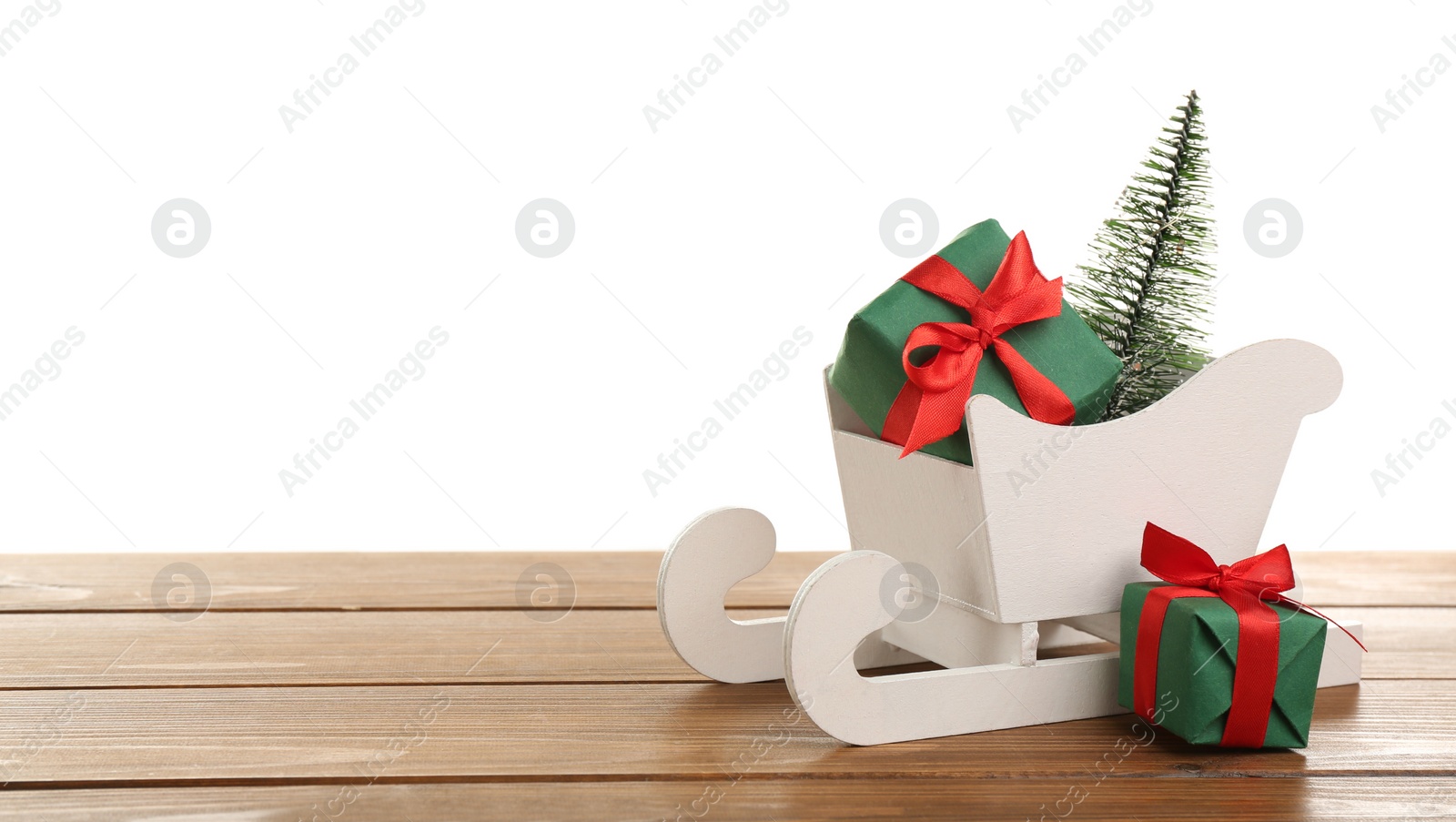 Photo of Small sleigh with Christmas gift boxes and decorative fir tree on wooden table. Space for text