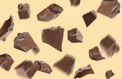 Delicious chocolate pieces falling on yellow background