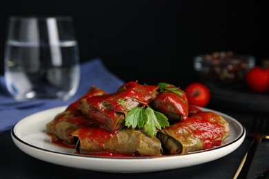 Photo of Delicious stuffed grape leaves with tomato sauce on black table