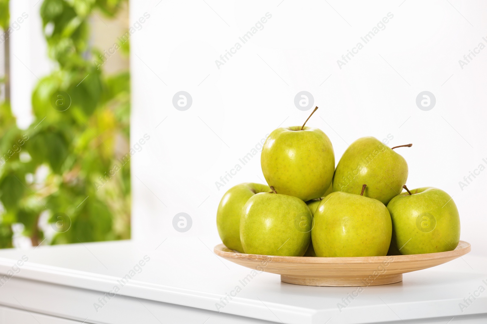 Photo of Plate with sweet green apples on commode in room, space for text