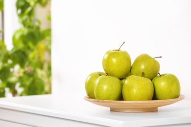 Plate with sweet green apples on commode in room, space for text