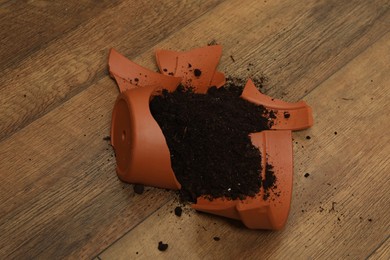 Photo of Broken terracotta flower pot with soil on wooden floor