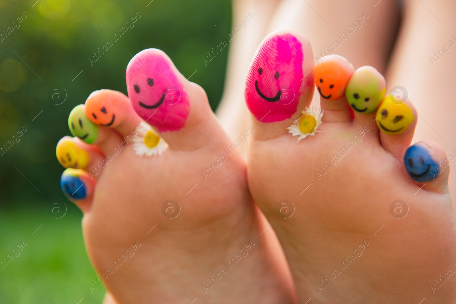 Photo of Teenage girl with chamomiles and smiling faces drawn on toes outdoors, closeup