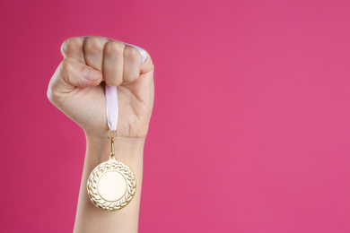 Woman holding golden medal on pink background, closeup. Space for design