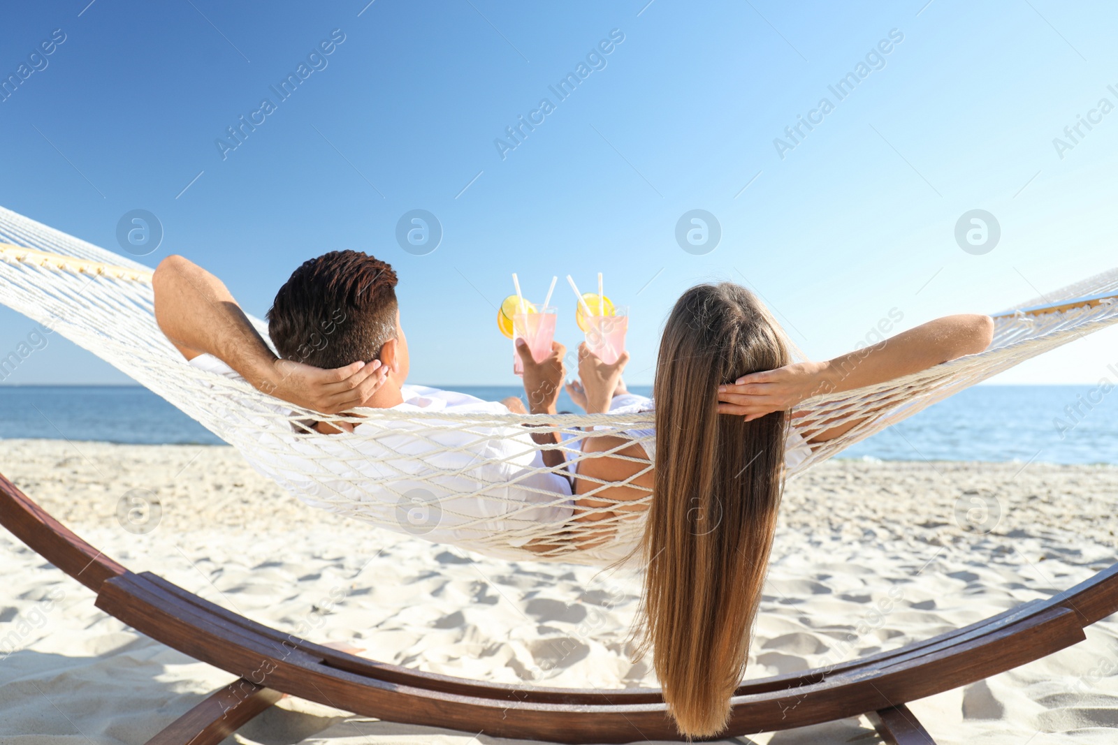 Photo of Couple with refreshing cocktails relaxing in hammock on beach