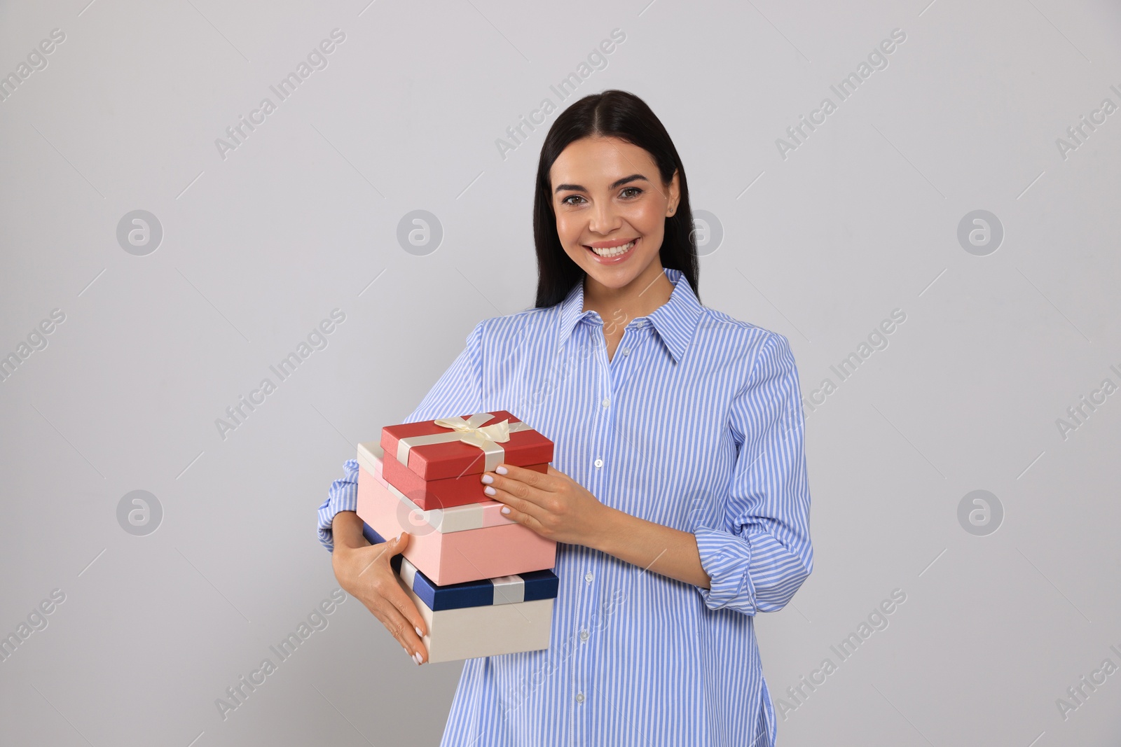 Photo of Happy young woman holding gift boxes on light grey background