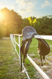 Photo of Leather horse saddle on wooden fence outdoors