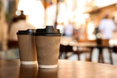 Photo of Cardboard takeaway coffee cups with plastic lids on wooden table in city, space for text