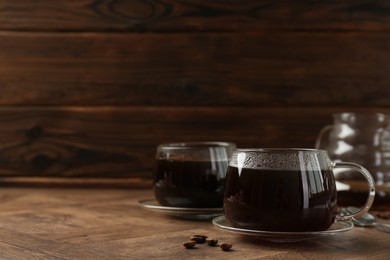 Hot coffee in glass cups and beans on wooden table, closeup. Space for text