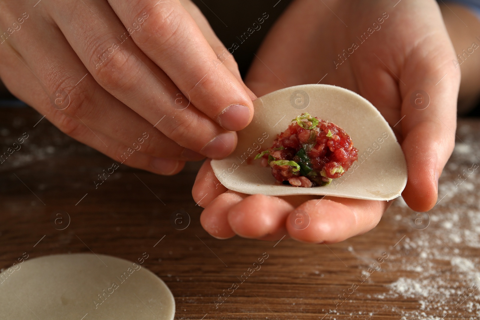 Photo of Woman making gyoza at wooden table, closeup