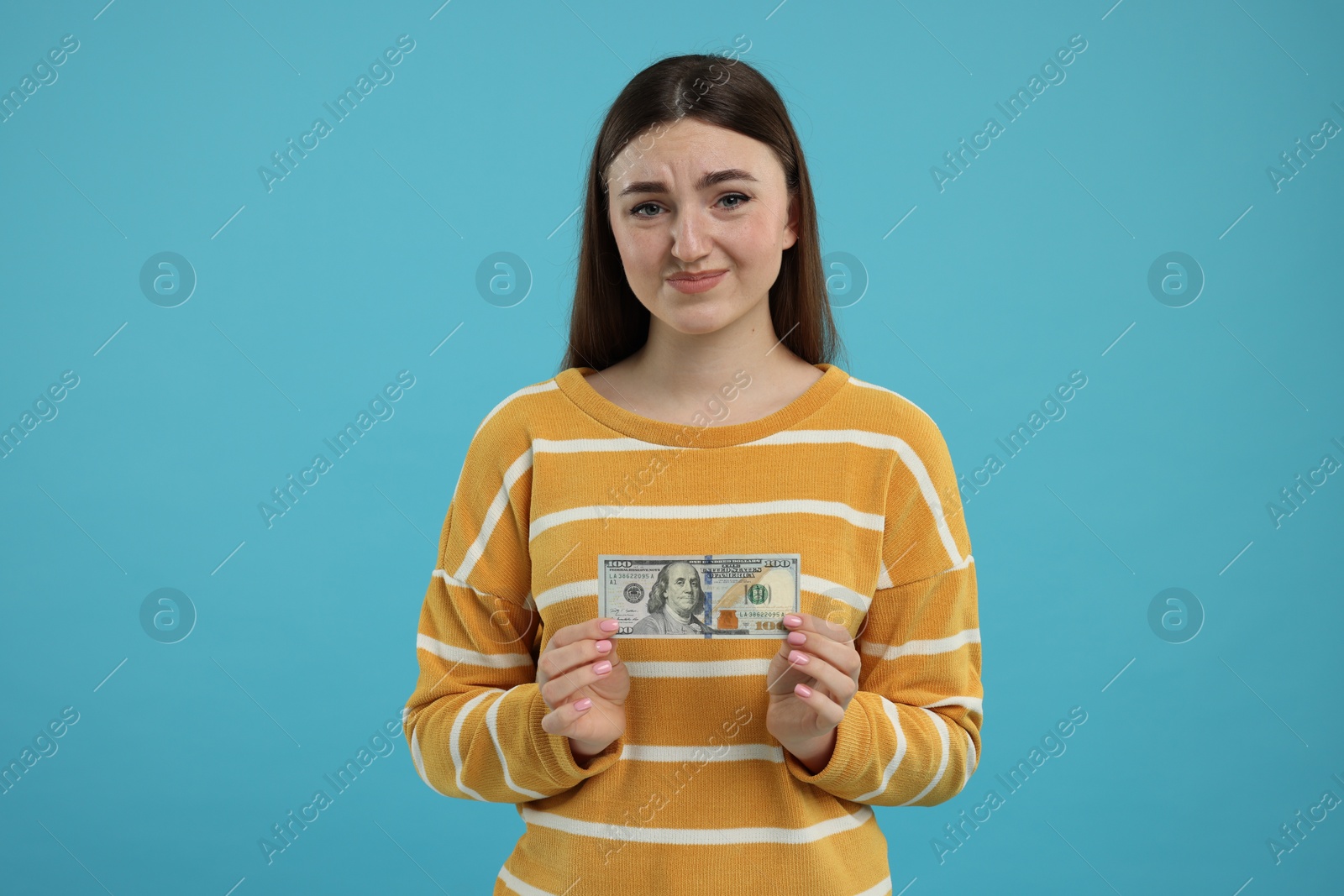 Photo of Sad woman with dollar banknote on light blue background