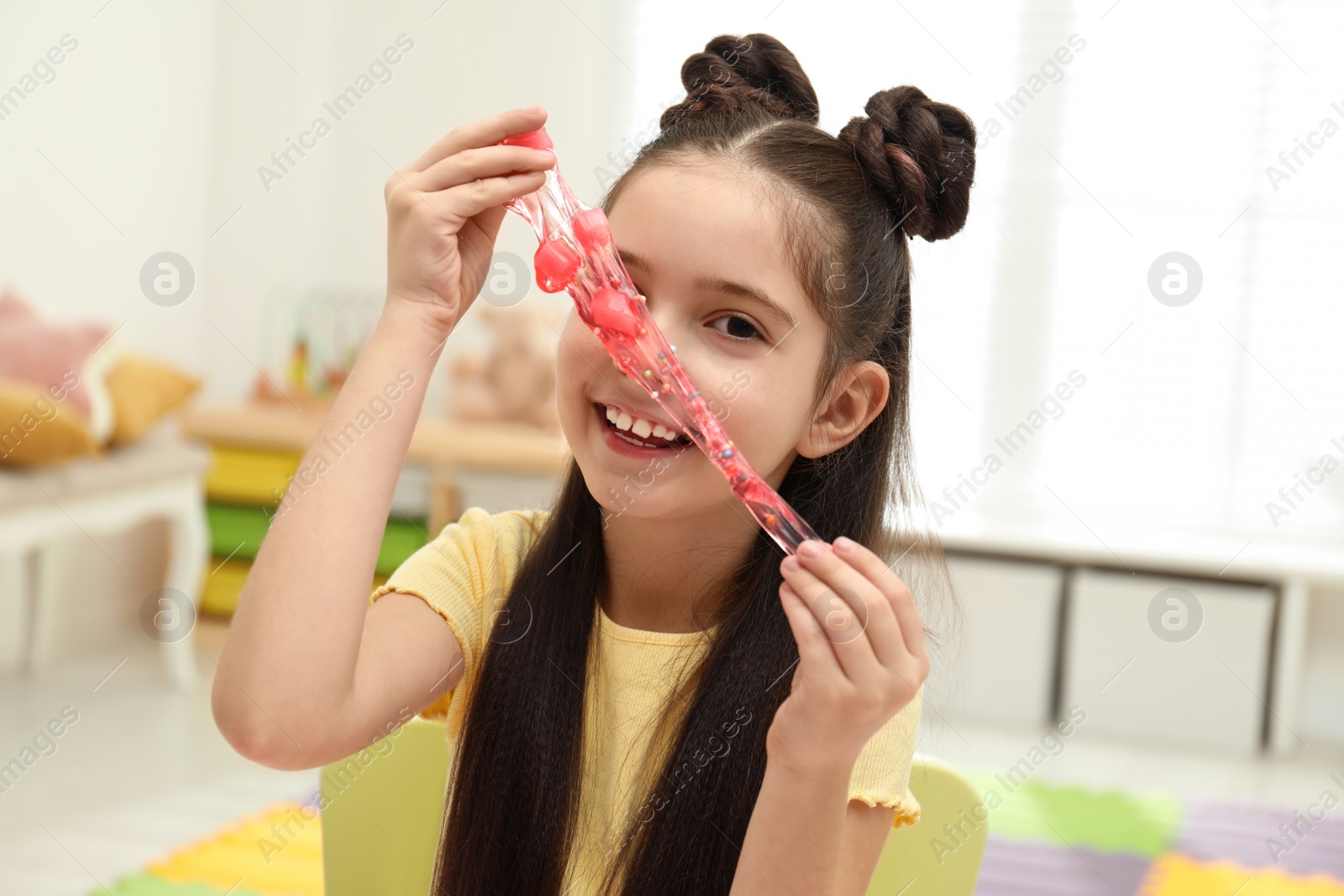Photo of Little girl playing with slime in room