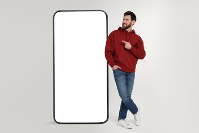 Man pointing at huge mobile phone with empty screen on grey background. Mockup for design