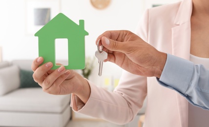 Young couple holding key and house model, closeup. Real estate agent services