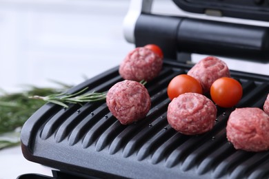 Photo of Meatballs, tomatoes and rosemary on electric grill, closeup