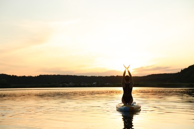 Photo of Woman practicing yoga on SUP board on river at sunset, back view