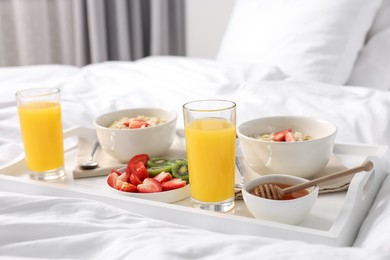 Photo of Tasty breakfast served in bed. Oatmeal, juice, fruits and honey on tray