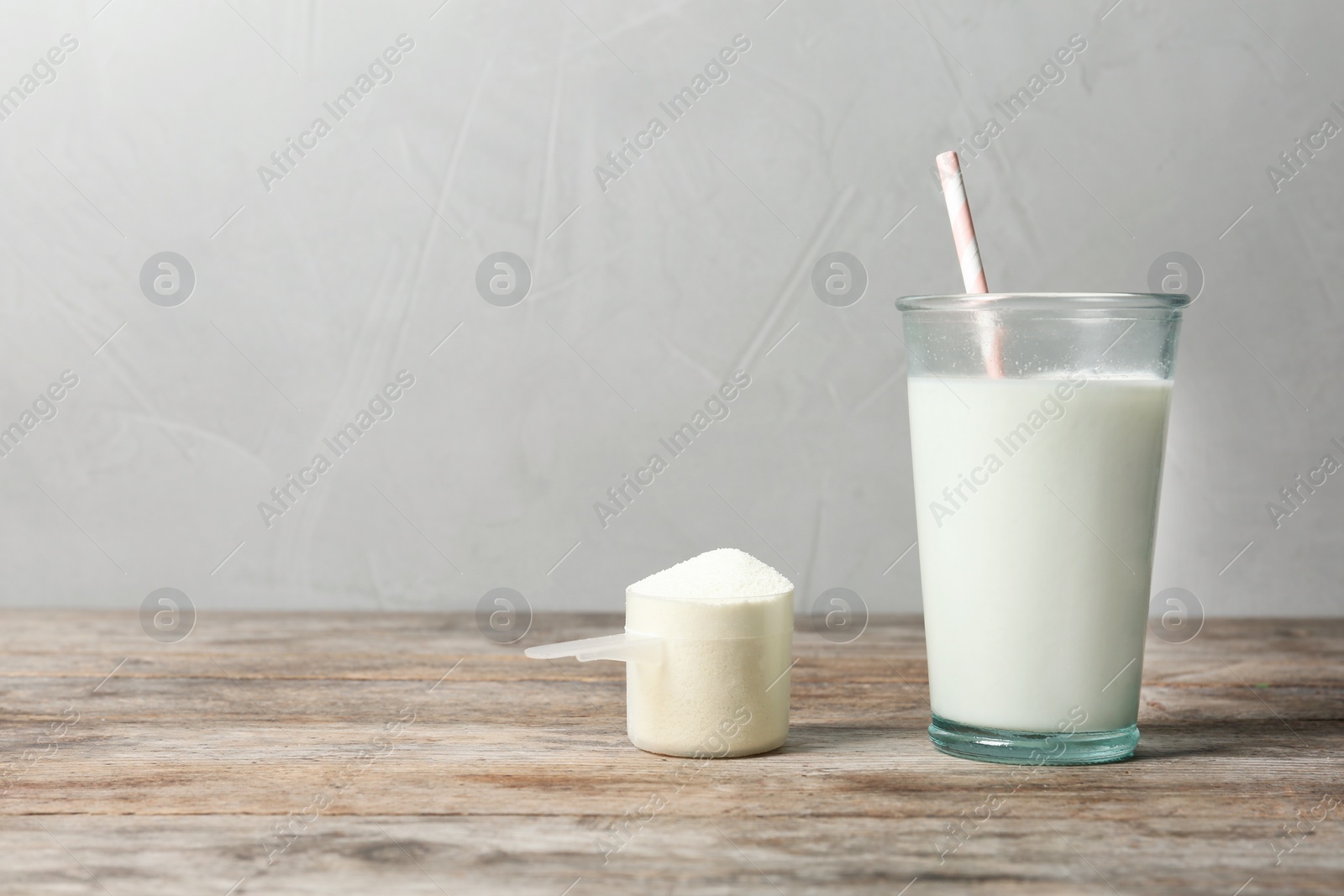 Photo of Glass of protein shake and scoop with powder on table. Space for text