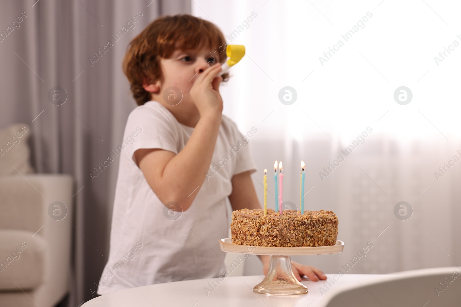 Photo of Birthday celebration. Cute boy with party blower at table with tasty cake indoors