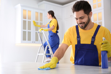 Professional young janitor cleaning table in kitchen