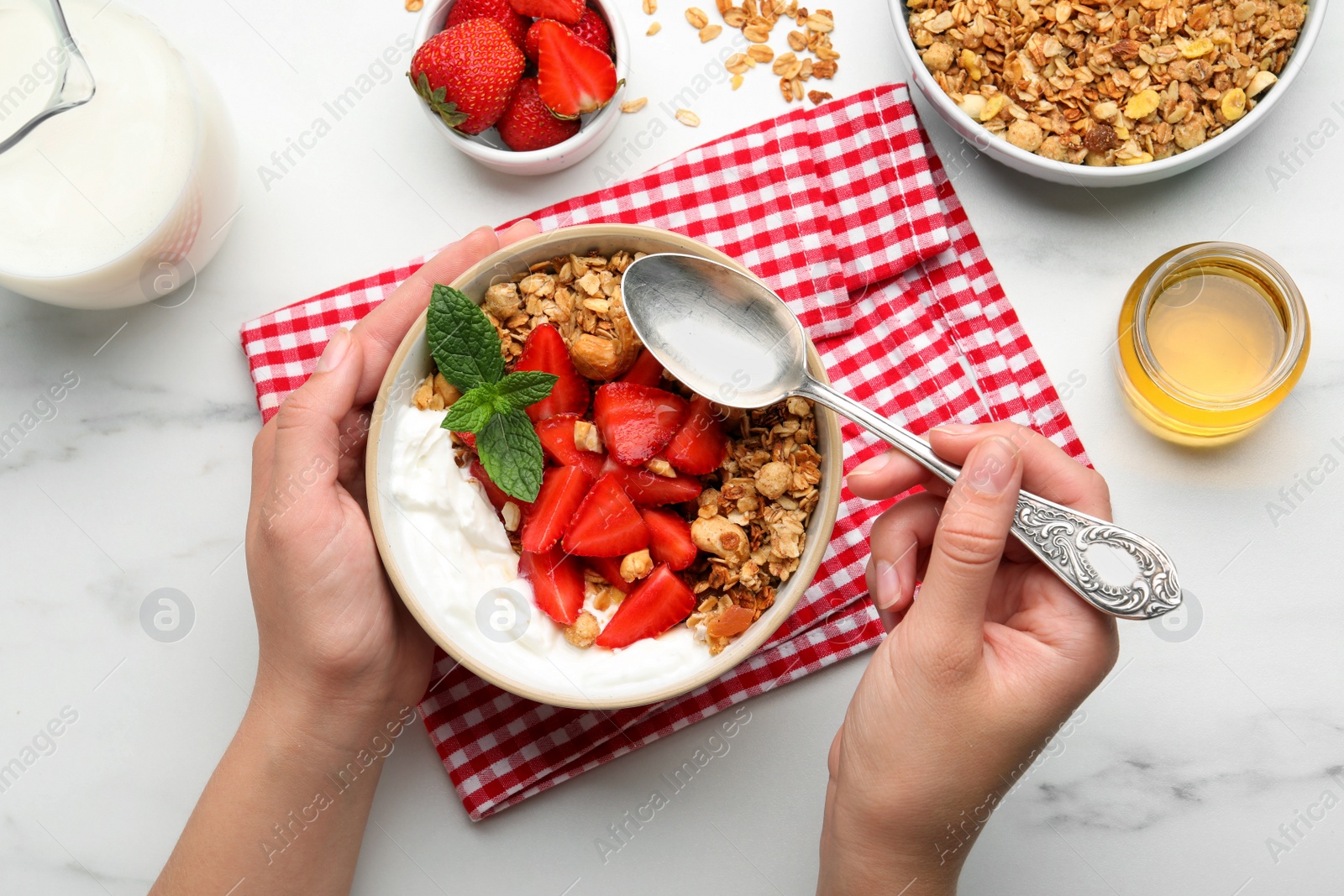 Photo of Woman eating tasty granola at white table, top view. Healthy meal