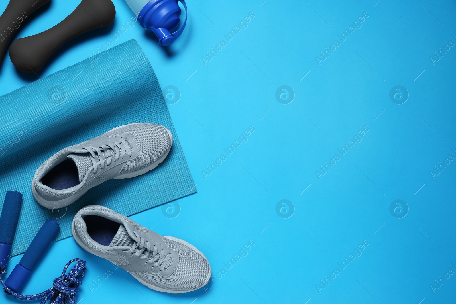 Photo of Exercise mat, shoes, dumbbells, shaker and skipping rope on turquoise background, flat lay. Space for text