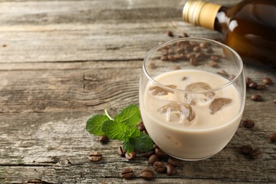 Coffee cream liqueur in glass, mint and beans on wooden table, space for text