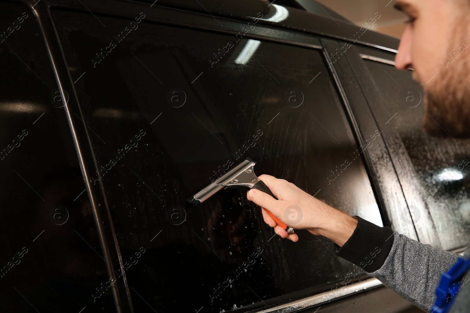 Photo of Worker washing tinted car window in shop, closeup