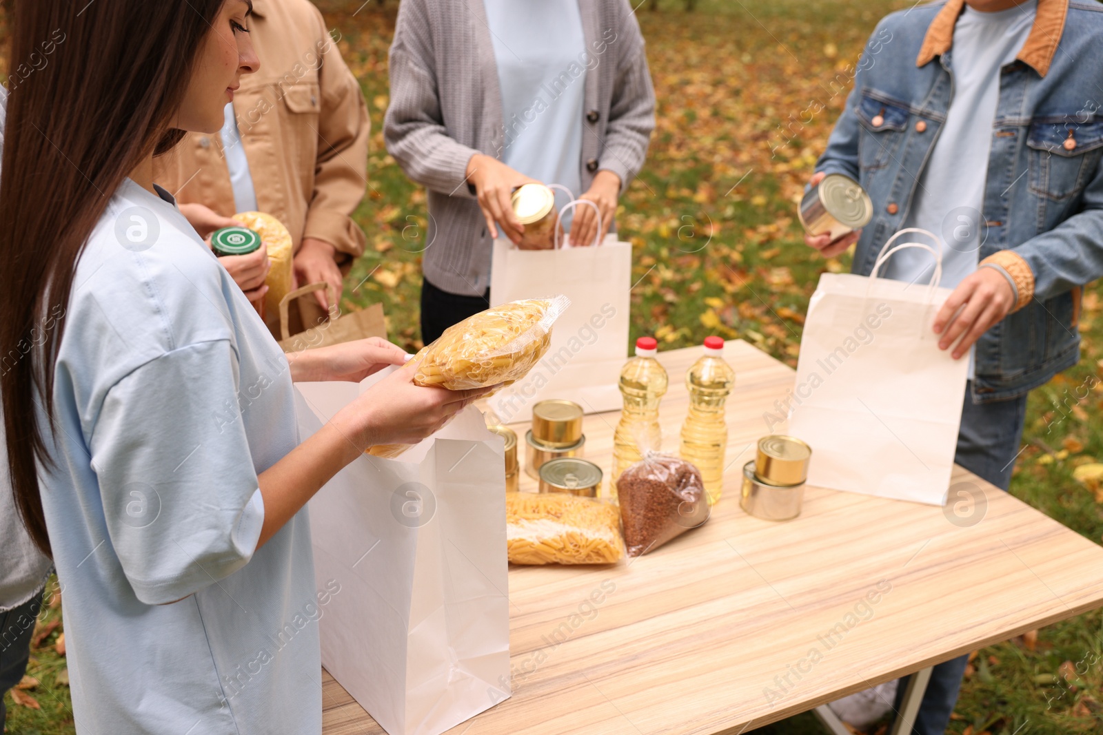 Photo of Group of volunteers packing food products at table outdoors, closeup