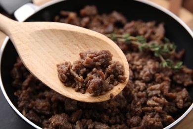 Photo of Holding spoon with fried ground meat over frying pan, closeup