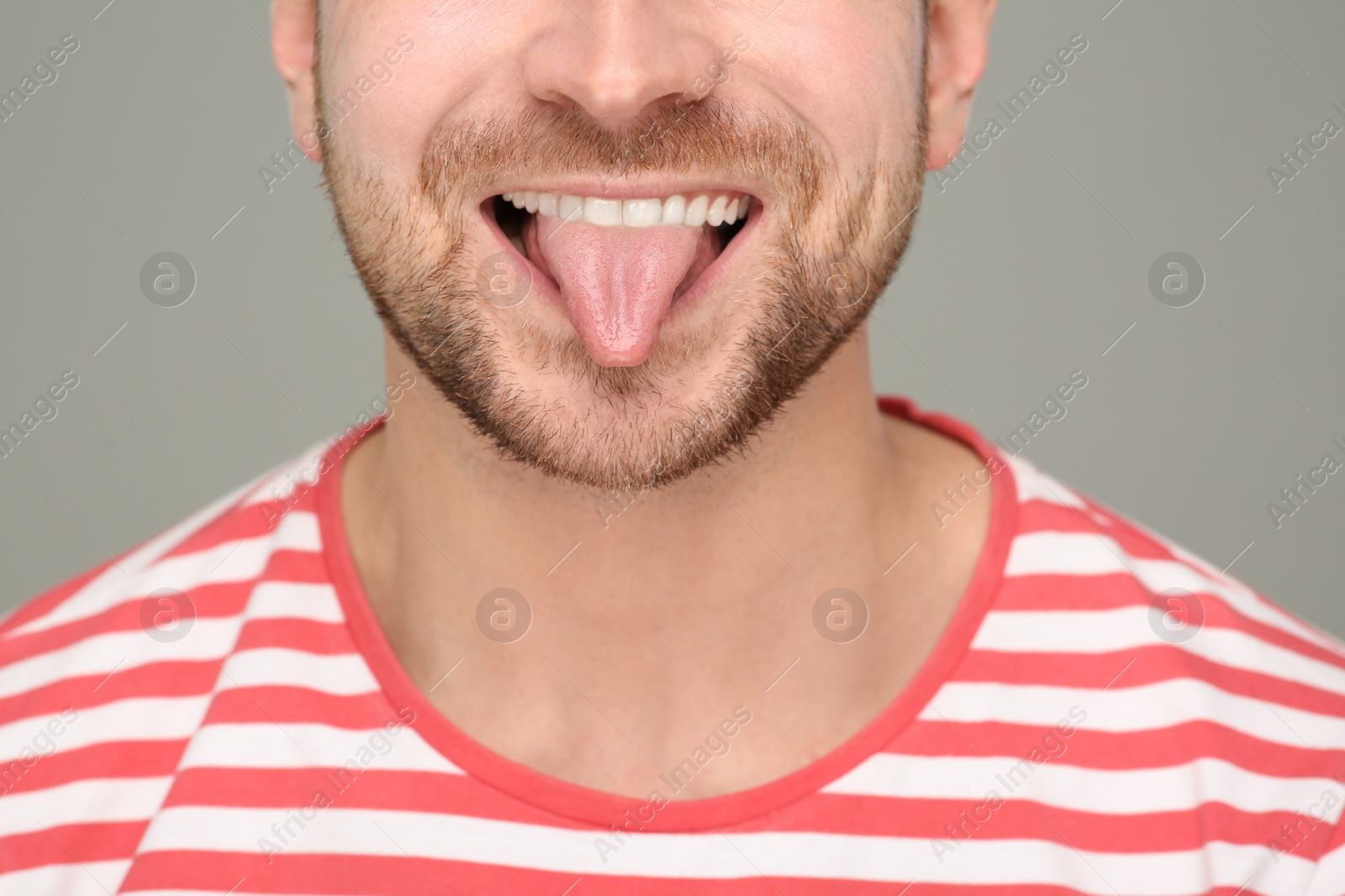 Photo of Man showing his tongue on grey background, closeup