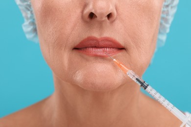 Photo of Senior woman getting lips injection on light blue background, closeup. Cosmetic surgery