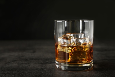 Photo of Golden whiskey in glass with ice cubes on table. Space for text