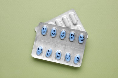 Photo of Different antidepressants with happy emoticons on light green background, flat lay