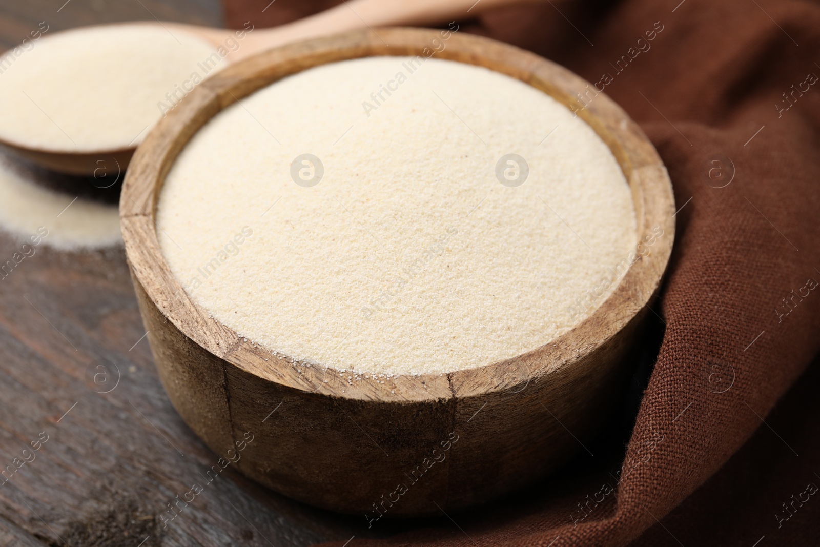 Photo of Uncooked organic semolina in bowl and spoon on wooden table, closeup