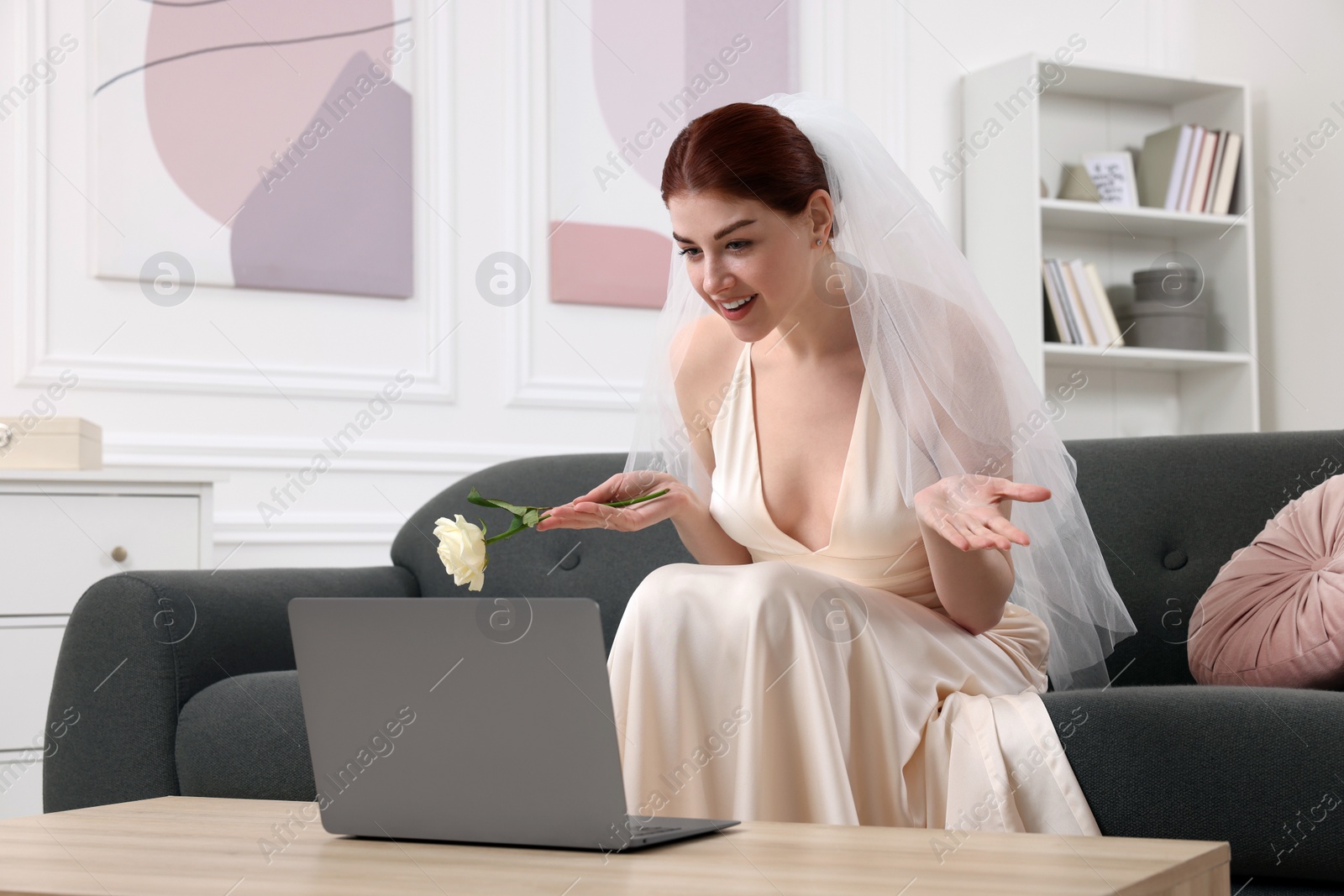 Photo of Happy bride with rose having online video chat via laptop in living room