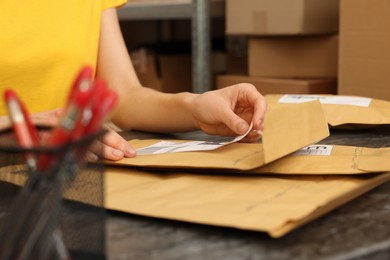 Photo of Post office worker sticking barcode on parcel at counter indoors, closeup