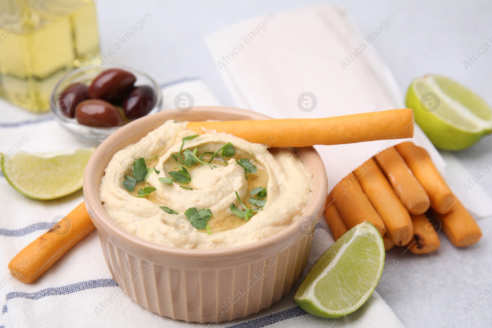 Photo of Delicious hummus with grissini sticks, lime and olives on light grey table