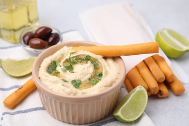 Delicious hummus with grissini sticks, lime and olives on light grey table