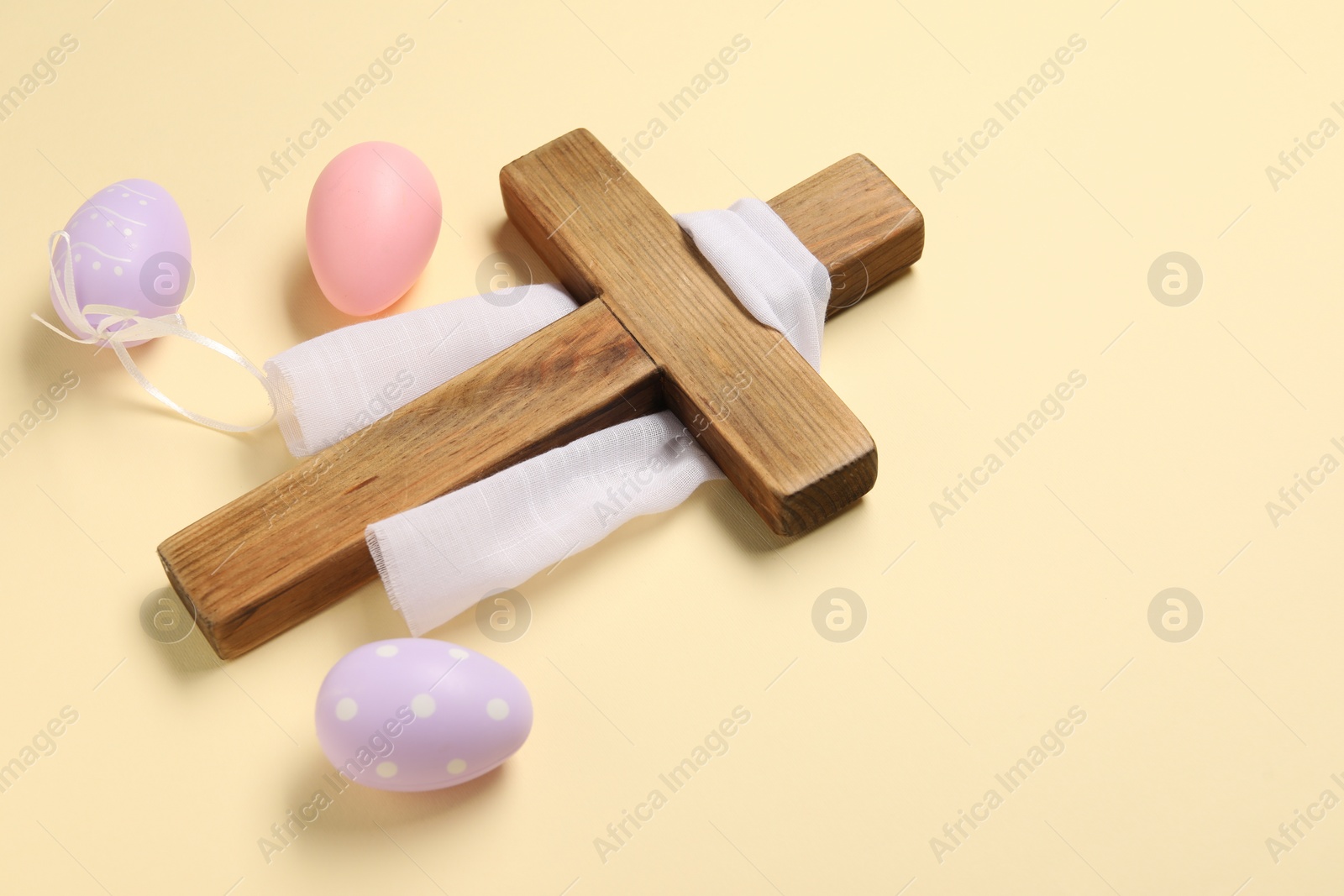 Photo of Wooden cross, white cloth and painted Easter eggs on beige background