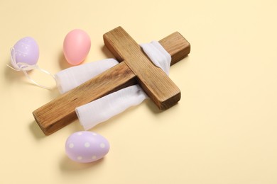 Photo of Wooden cross, white cloth and painted Easter eggs on beige background