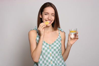 Young woman with glass of lemon water on light background